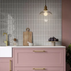Earth Cotton Grey 65x130mm glossy grey tiles with irregular edges installed as a kitchen splashback above pink cabinets and brass tap.
