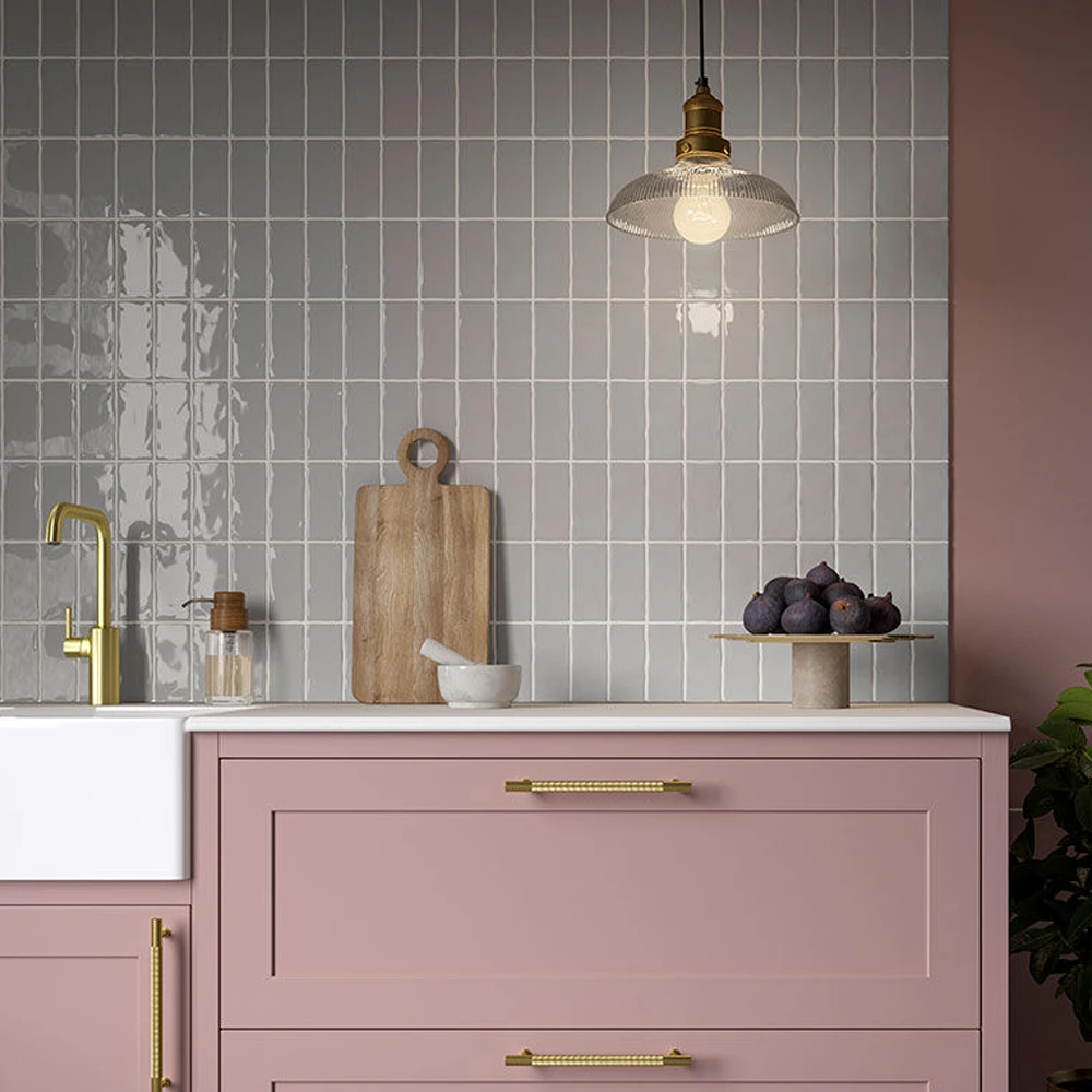 Earth Cotton Grey 65x130mm glossy grey tiles with irregular edges installed as a kitchen splashback above pink cabinets and brass tap.